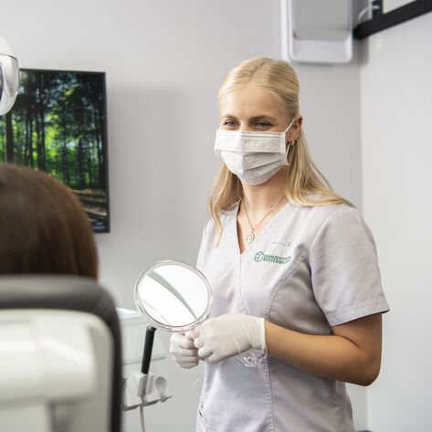 Zahnmedizinische Fachangestellte steht vor Patientin und hält einen Spiegel